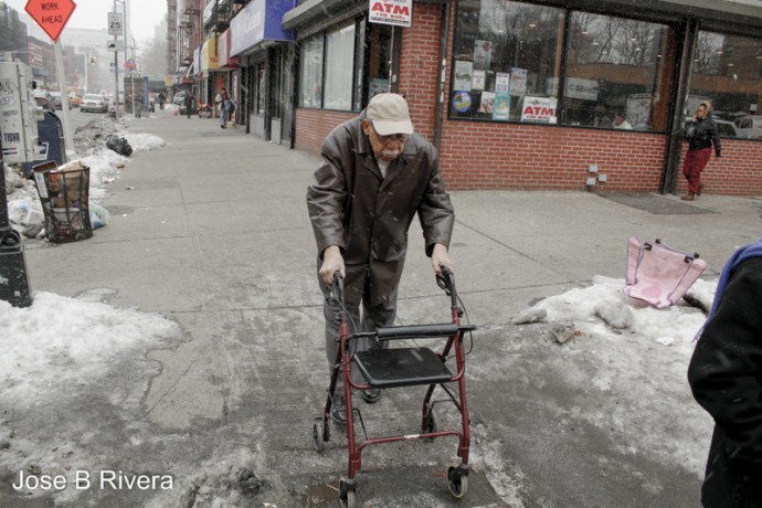 Elderly gentleman using walker to navigate icy street.
