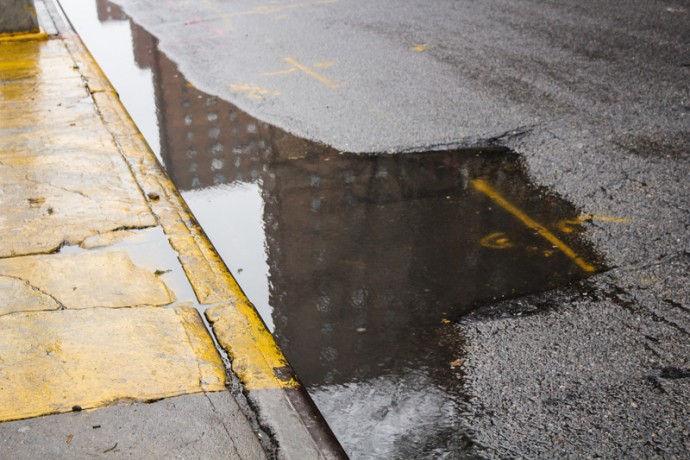 A water puddle reflects the image of the Lehman Houses at East 110th Street near Madison Avenue.