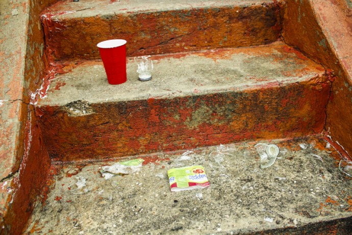 A red plastic cup with a shattered glass bottle underneath it. Taken at East 110th Street between Madison and Park Avenues.