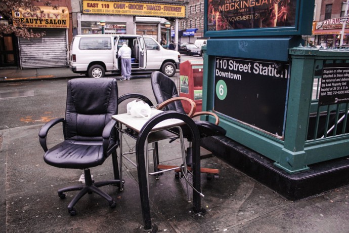 Two Chairs and a table at the entrance to the East 110th Street Subway.