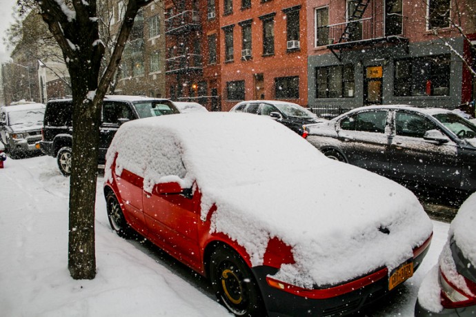 Red car is covered in snow at East 111th Street between Second and Third Avenues.