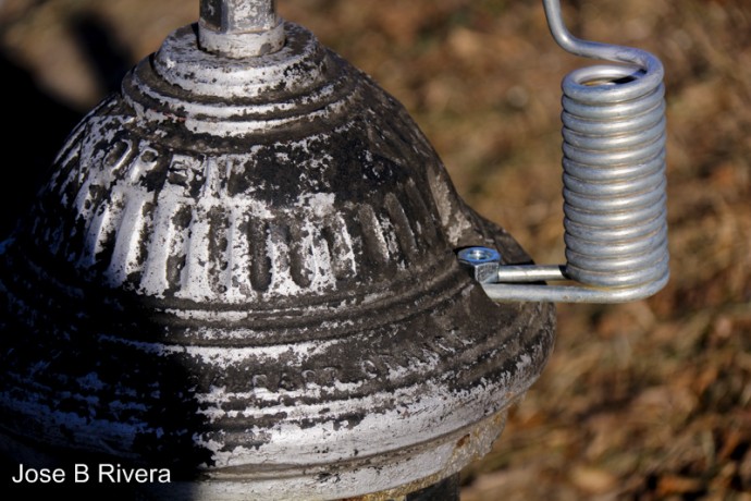 This is close up of one of the hydrants in Central Park. The coils is the bottom of a metal sign holder which alerts the authorities just where the hydrants are.