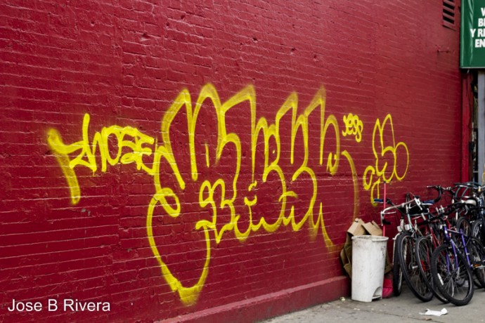 Red painted wall with yellow graffiti on it. Bicycles rest against the wall.