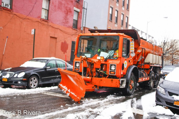 A big orange snow plow going down East 110th Street heading East toward Second Avenue.